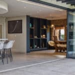 Thumbnail of http://Modern%20open-concept%20living%20space%20with%20a%20kitchen%20island,%20bar%20stools,%20and%20a%20dining%20area.%20Sliding%20glass%20doors%20lead%20to%20a%20tiled%20patio.%20Dark%20shelving%20contrasts%20with%20light%20walls%20and%20flooring.