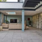 Thumbnail of http://Modern%20open-plan%20living%20room%20with%20beige%20couches,%20wall-mounted%20TV,%20and%20glass%20folding%20doors%20leading%20to%20a%20patio.%20Walls%20are%20painted%20in%20green%20and%20gray%20with%20decorative%20plants%20and%20art.