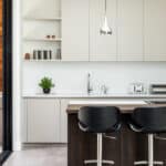 Thumbnail of http://Modern%20kitchen%20with%20white%20cabinets,%20a%20sink,%20and%20countertop%20appliances.%20Three%20black%20bar%20stools%20at%20a%20dark%20wooden%20island.%20Hanging%20light%20fixtures%20and%20a%20potted%20plant%20add%20decor.