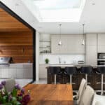 Thumbnail of http://Modern%20kitchen%20with%20a%20skylight,%20a%20wooden%20dining%20table,%20bar%20stools%20at%20an%20island,%20built-in%20appliances,%20and%20an%20outdoor%20area%20with%20a%20grill.