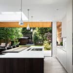 Thumbnail of http://Modern%20kitchen%20with%20an%20island,%20pendant%20lights,%20and%20white%20cabinetry.%20Large%20sliding%20doors%20open%20to%20a%20garden%20with%20trees%20and%20greenery.%20Dining%20table%20and%20chairs%20are%20visible%20on%20the%20left.