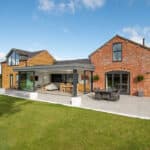 Thumbnail of http://A%20modern%20house%20exterior%20featuring%20a%20blend%20of%20brick%20and%20glass,%20with%20a%20spacious%20patio%20and%20outdoor%20seating.%20The%20adjacent%20lawn%20is%20accessible%20through%20sleek%20sliding%20doors%20by%20HBD%20Systems,%20seamlessly%20merging%20indoor%20and%20outdoor%20spaces%20under%20a%20clear%20sky.