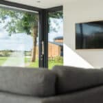 Thumbnail of http://The%20living%20room%20features%20a%20gray%20sofa%20and%20large%20windows,%20complemented%20by%20a%20mounted%20flat-screen%20TV%20on%20the%20wall.%20Sliding%20doors%20by%20HBD%20Systems%20open%20to%20reveal%20a%20lush%20green%20lawn,%20seamlessly%20blending%20indoor%20comfort%20with%20outdoor%20beauty.