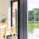 Thumbnail of http://Close-up%20of%20a%20slightly%20open%20sliding%20glass%20door%20by%20HBD%20Systems,%20offering%20a%20glimpse%20into%20a%20bright%20dining%20area.%20Inside,%20there's%20a%20table,%20chairs,%20a%20colorful%20painting,%20and%20a%20vase%20with%20flowers.%20The%20space%20beautifully%20connects%20to%20the%20garden%20outside%20through%20the%20glazed%20extension.