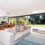 Thumbnail of http://Modern%20open-plan%20living%20space%20with%20a%20sofa,%20dining%20area,%20and%20large%20sliding%20glass%20doors%20by%20HBD%20Systems%20leading%20to%20a%20garden%20with%20a%20basketball%20hoop.%20The%20room%20features%20a%20light%20color%20scheme%20and%20contemporary%20decor.