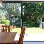 Thumbnail of http://A%20modern%20dining%20area%20with%20elegant%20wooden%20furniture%20opens%20to%20a%20backyard%20through%20sleek%20sliding%20doors%20by%20HBD%20Systems.%20The%20charming%20backyard%20features%20a%20large%20tree,%20a%20cozy%20shed,%20and%20a%20goalpost,%20creating%20an%20inviting%20space%20for%20relaxation%20and%20play.