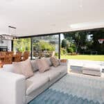 Thumbnail of http://Modern%20open-plan%20living%20room%20featuring%20a%20gray%20sofa,%20patterned%20cushions,%20and%20a%20wooden%20dining%20set.%20Large%20sliding%20doors%20by%20HBD%20Systems%20lead%20to%20a%20garden%20complete%20with%20a%20basketball%20hoop%20and%20soccer%20goal.