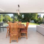 Thumbnail of http://Modern%20open-plan%20kitchen%20and%20dining%20area%20featuring%20a%20wooden%20table%20and%20chairs,%20light%20gray%20tiles,%20and%20floor-to-ceiling%20sliding%20doors%20by%20HBD%20Systems.%20These%20doors%20lead%20to%20a%20garden%20equipped%20with%20a%20patio,%20trampoline,%20and%20basketball%20hoop.