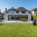 Thumbnail of http://Rear%20view%20of%20a%20modern%20house%20featuring%20HBD%20Systems'%20sleek%20sliding%20doors,%20a%20patio%20area%20with%20dining%20set,%20barbecue,%20and%20a%20spacious%20green%20lawn%20under%20a%20clear%20blue%20sky.