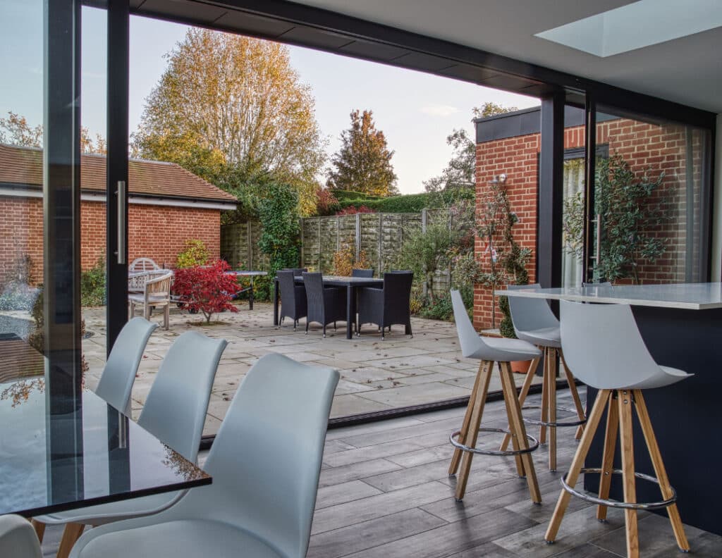 Modern dining area with glass doors opening to a patio. The outdoor space includes a table, chairs, and surrounding greenery.