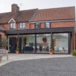 Thumbnail of http://A%20red%20brick%20house%20with%20a%20modern%20glass%20extension,%20featuring%20a%20patio%20area%20with%20outdoor%20seating%20and%20potted%20plants.