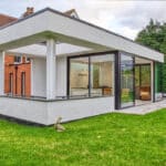 Thumbnail of http://Modern%20glass%20and%20white%20concrete%20extension%20on%20a%20traditional%20red-brick%20house,%20with%20a%20green%20lawn%20and%20surrounding%20trees.