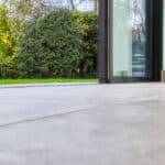 Thumbnail of http://View%20from%20a%20tiled%20floor%20through%20an%20open%20glass%20door%20to%20a%20garden%20with%20green%20grass,%20bushes,%20and%20a%20wooden%20fence.