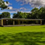 Thumbnail of http://Modern,%20single-story%20glass%20and%20wood%20building%20surrounded%20by%20a%20large,%20lush%20green%20lawn%20and%20trees%20under%20a%20partly%20cloudy%20sky.