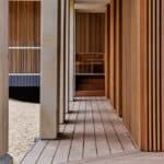 Thumbnail of http://Wooden%20hallway%20with%20vertical%20slat%20walls%20and%20a%20matching%20floor.%20Staircase%20at%20the%20end%20leading%20to%20a%20wooden%20chair.%20Light%20filters%20in%20from%20the%20open%20side.