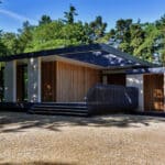 Thumbnail of http://Modern%20house%20with%20flat%20roof%20and%20large%20windows,%20surrounded%20by%20trees.%20The%20building%20features%20wood%20accents%20and%20a%20gravel%20driveway.