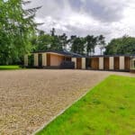 Thumbnail of http://Modern%20single-story%20house%20with%20large%20windows,%20surrounded%20by%20trees%20and%20a%20gravel%20driveway,%20next%20to%20a%20well-maintained%20lawn.