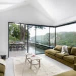 Thumbnail of http://Modern%20living%20room%20with%20green%20sofas,%20a%20wood-burning%20stove,%20large%20glass%20doors,%20and%20a%20view%20of%20an%20outdoor%20dining%20area%20and%20scenic%20landscape.