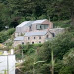 Thumbnail of http://A%20rustic%20stone%20house%20with%20a%20modern%20wooden%20extension%20is%20nestled%20in%20a%20lush,%20green%20hillside.%20Trees%20surround%20the%20property,%20and%20a%20white%20building%20is%20partially%20visible%20in%20the%20foreground.