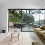 Thumbnail of http://Modern%20living%20room%20with%20green%20sofas,%20a%20wooden%20table,%20and%20a%20fireplace.%20Large%20glass%20doors%20open%20to%20a%20patio%20with%20outdoor%20furniture,%20overlooking%20a%20natural%20landscape%20with%20trees%20and%20hills.