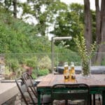 Thumbnail of http://Two%20bottles%20of%20beer%20on%20a%20rustic%20outdoor%20table%20with%20metal%20chairs,%20surrounded%20by%20greenery%20and%20stone%20walls,%20under%20a%20cloudy%20sky.