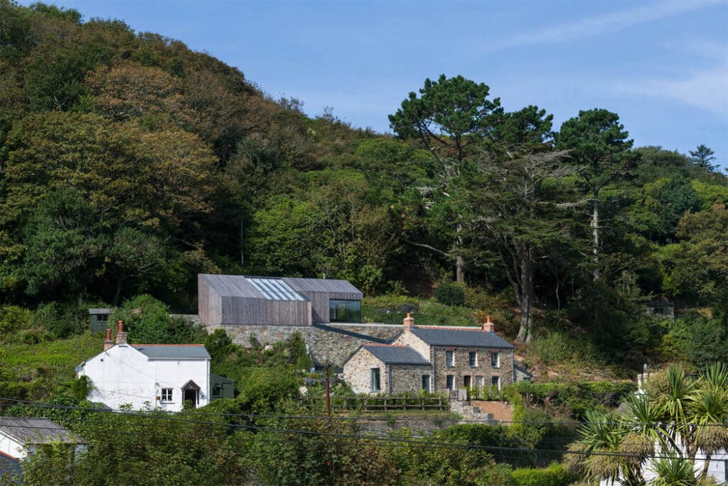 Houses with stone and wooden exteriors surrounded by trees on a hillside under a clear blue sky.
