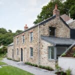 Thumbnail of http://A%20stone%20cottage%20with%20two%20chimneys,%20surrounded%20by%20greenery.%20The%20building%20has%20gray%20roofing%20and%20a%20path%20lined%20with%20gravel%20and%20plants.