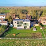 Thumbnail of http://A%20large%20modern%20house%20with%20a%20glass%20facade%20is%20situated%20in%20a%20rural%20area,%20surrounded%20by%20traditional%20homes,%20green%20fields,%20and%20trees.