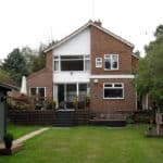 Thumbnail of http://Two-story%20brick%20house%20with%20a%20large%20lawn,%20a%20raised%20patio%20with%20chairs%20on%20the%20left,%20and%20a%20hedge%20on%20the%20right.%20A%20small%20shed%20is%20partially%20visible%20on%20the%20right.