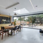 Thumbnail of http://Modern%20kitchen%20and%20dining%20area%20with%20black%20and%20gold%20cabinets,%20wooden%20table,%20and%20sliding%20glass%20doors%20leading%20to%20a%20patio%20and%20garden.