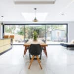 Thumbnail of http://Modern%20kitchen%20and%20dining%20area%20with%20a%20wooden%20table,%20black%20chairs,%20gold%20cabinets,%20and%20large%20glass%20doors%20leading%20to%20a%20garden.%20Daylight%20illuminates%20the%20marble%20floor%20and%20lounge%20area.