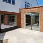 Thumbnail of http://A%20modern%20brick%20house%20with%20large%20glass%20sliding%20doors%20and%20windows,%20leading%20to%20a%20spacious%20tiled%20patio%20under%20a%20clear%20blue%20sky.