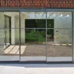 Thumbnail of http://Sliding%20glass%20patio%20doors%20with%20grid-pattern%20frames%20on%20a%20brick%20wall,%20reflecting%20a%20green%20outdoor%20area.