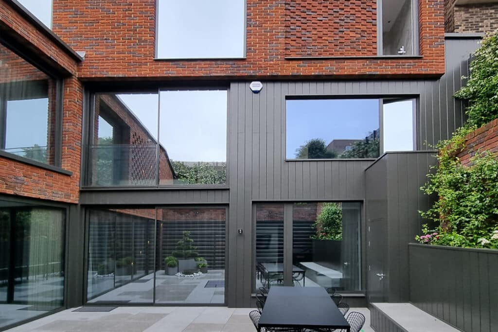 Modern brick and glass building exterior with large windows and a patio featuring a long table and chairs.