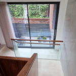 Thumbnail of http://View%20from%20a%20staircase%20landing%20showing%20a%20glass%20door%20leading%20to%20a%20patio%20with%20potted%20plants%20and%20a%20small%20table%20with%20chairs.%20A%20brick%20wall%20with%20greenery%20is%20visible%20outside.