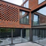 Thumbnail of http://Modern%20architectural%20exterior%20featuring%20brick%20latticework,%20large%20glass%20windows,%20and%20a%20courtyard%20with%20potted%20plants%20and%20outdoor%20seating.