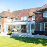 Thumbnail of http://Large%20brick%20house%20with%20an%20open%20sunroom,%20expansive%20glass%20doors,%20and%20a%20spacious%20patio%20overlooking%20a%20manicured%20lawn.