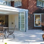 Thumbnail of http://A%20modern%20house%20exterior%20with%20large%20folding%20glass%20doors,%20leading%20to%20a%20spacious%20patio.%20Outdoor%20furniture%20and%20potted%20plants%20are%20arranged%20on%20the%20patio.