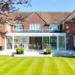 Thumbnail of http://A%20large%20brick%20house%20with%20a%20glass%20sunroom%20extension,%20surrounded%20by%20a%20well-maintained%20lawn%20and%20plant%20pots.