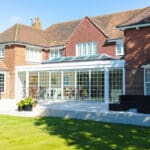 Thumbnail of http://A%20large%20brick%20house%20with%20a%20glass%20conservatory%20opens%20onto%20a%20patio,%20surrounded%20by%20a%20well-maintained%20lawn%20and%20potted%20plants.