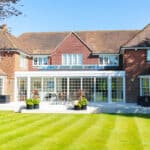 Thumbnail of http://A%20large%20brick%20house%20with%20multiple%20sections,%20featuring%20a%20glass%20conservatory%20and%20several%20windows,%20set%20against%20a%20well-maintained%20lawn%20and%20clear%20blue%20sky.