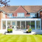 Thumbnail of http://Large%20brick%20house%20with%20a%20glass-enclosed%20patio,%20surrounded%20by%20a%20well-manicured%20lawn.%20Outdoor%20furniture%20is%20visible%20on%20the%20patio.