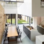 Thumbnail of http://Modern%20kitchen%20and%20dining%20area%20with%20a%20long%20table,%20black%20chairs,%20and%20light%20wood%20accents.%20Glass%20doors%20open%20to%20a%20grassy%20backyard%20where%20two%20people%20stand.%20Exposed%20brick%20walls%20and%20glass%20railing%20visible.