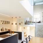 Thumbnail of http://Modern%20kitchen%20with%20black%20and%20white%20cabinetry,%20island%20with%20stovetop,%20pendant%20lights,%20and%20dining%20table.%20Stairs%20lead%20to%20a%20bright,%20open%20living%20area%20with%20a%20large%20window%20and%20a%20brick%20accent%20wall.