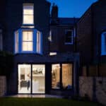 Thumbnail of http://Modern%20extension%20with%20large%20glass%20doors%20on%20a%20traditional%20brick%20townhouse,%20interior%20warmly%20lit,%20viewed%20from%20the%20backyard%20at%20dusk.