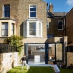 Thumbnail of http://Two%20children%20run%20in%20the%20yard%20of%20a%20brick%20house%20with%20large%20glass%20doors%20and%20windows.%20The%20house%20features%20a%20modern%20extension%20and%20a%20small%20garden%20area%20surrounded%20by%20a%20brick%20and%20fence%20boundary.