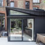 Thumbnail of http://Modern%20glass%20extension%20on%20a%20brick%20home%20features%20sliding%20doors.%20Inside,%20a%20dining%20table%20with%20chairs%20is%20visible.%20A%20wooden%20bench%20sits%20outside%20on%20a%20paved%20area.