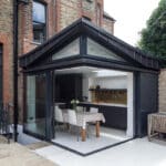 Thumbnail of http://Modern%20kitchen%20extension%20with%20glass%20walls%20attached%20to%20a%20brick%20house,%20featuring%20a%20dining%20table%20with%20a%20checkered%20tablecloth%20and%20chairs%20inside.