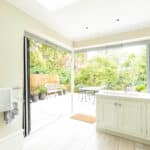 Thumbnail of http://Bright%20kitchen%20with%20open%20bi-fold%20doors%20leading%20to%20a%20patio.%20White%20cabinets%20and%20a%20light%20wood%20floor%20are%20visible.%20The%20patio%20features%20outdoor%20furniture%20and%20is%20surrounded%20by%20greenery.