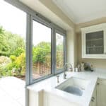 Thumbnail of http://A%20bright%20kitchen%20with%20cream%20cabinets%20and%20a%20sink;%20large%20glass%20doors%20open%20to%20a%20garden%20patio%20with%20table%20and%20chairs,%20surrounded%20by%20greenery.